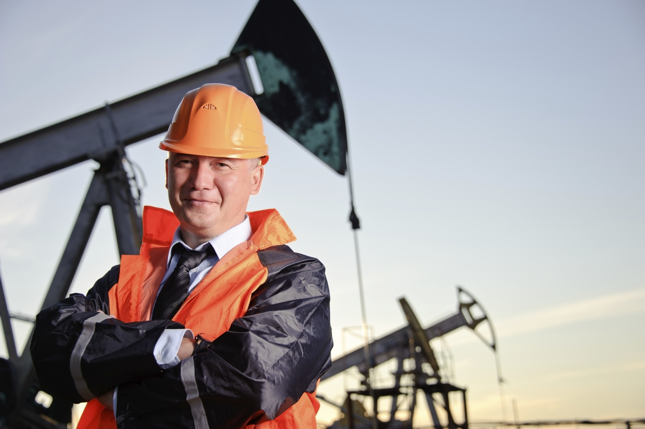 Engineer in an Oil field Oil worker in orange uniform and helmet on of background the pump jack and sunset sky.